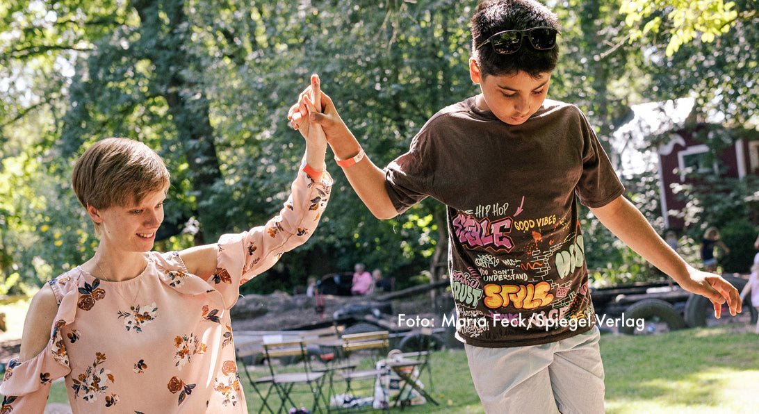Eine Mentorin (Balu) holft Ihrem Mentee (Mogli) beim Balancieren auf einem Spielplatz