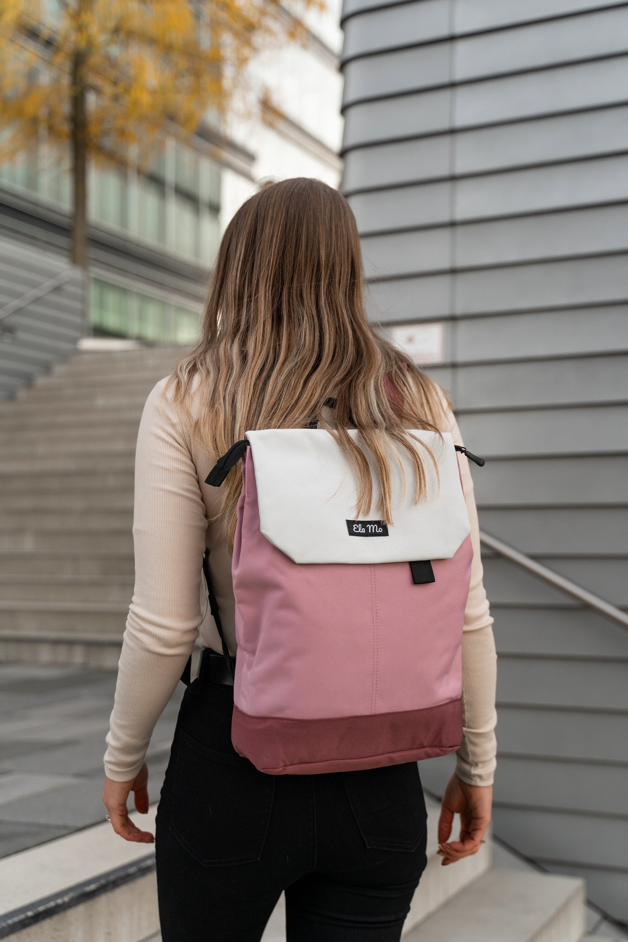 Ela Mo™ Daypack Rucksack | Strawberry Cream. Eine Frau mit dem rosa Rucksack auf der Straße.