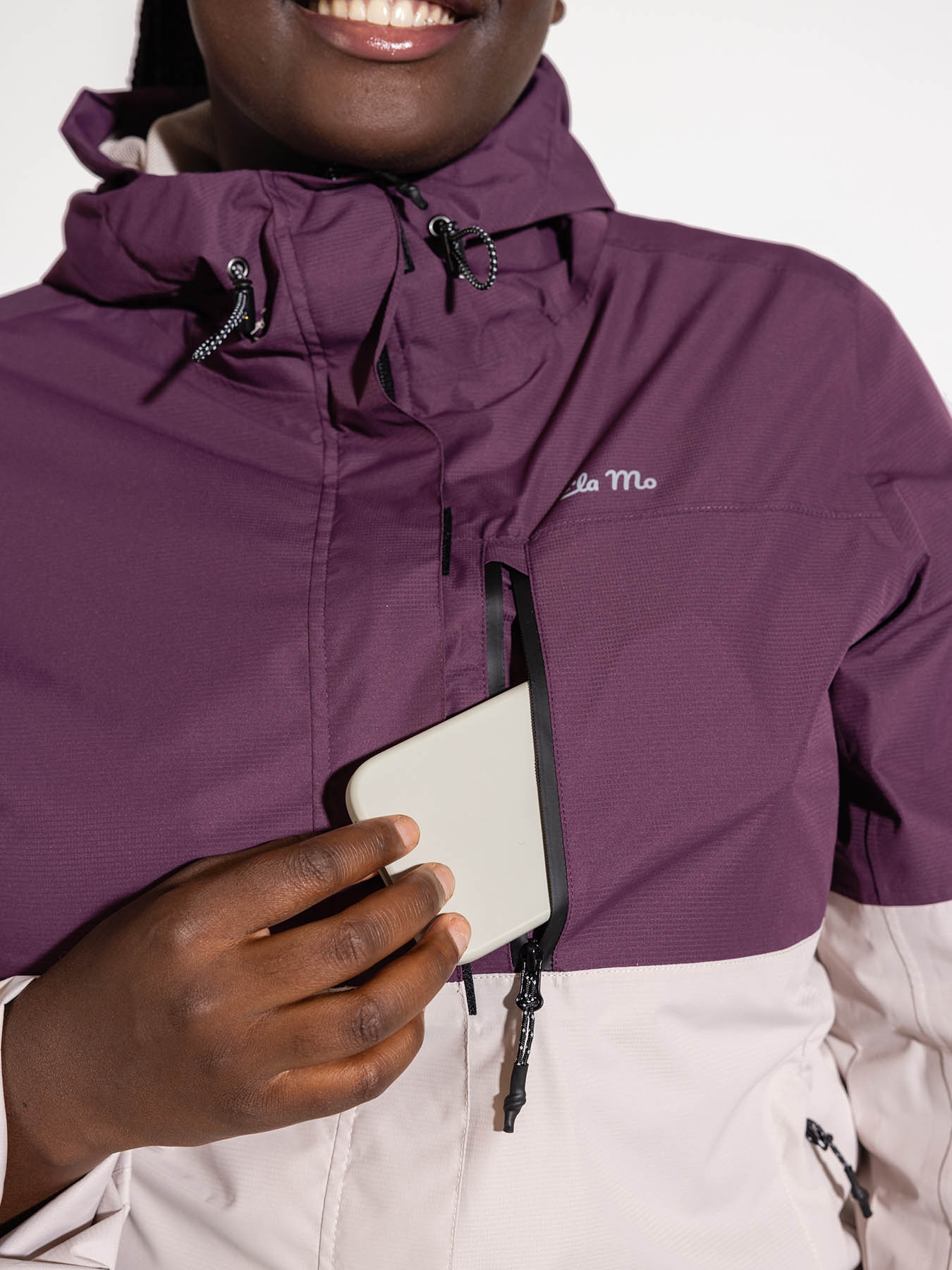 Ela Mo™ Regenjacke | Grape. Frau in Regenjacke mit einer seitlichen Handytasche, die durch Reißverschluss geschützt ist.