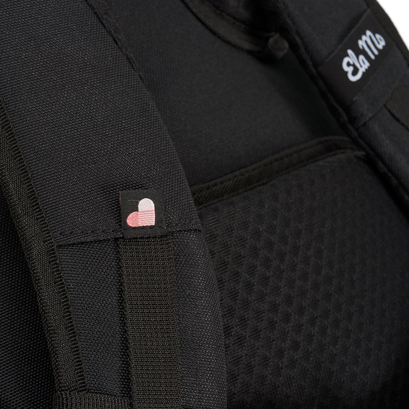 Ela Mo™ Everywhere Daypack | Black. Schulterriemen des schwarzen Rucksacks mit kleinen Herzchen und Herstellerlogo darauf.