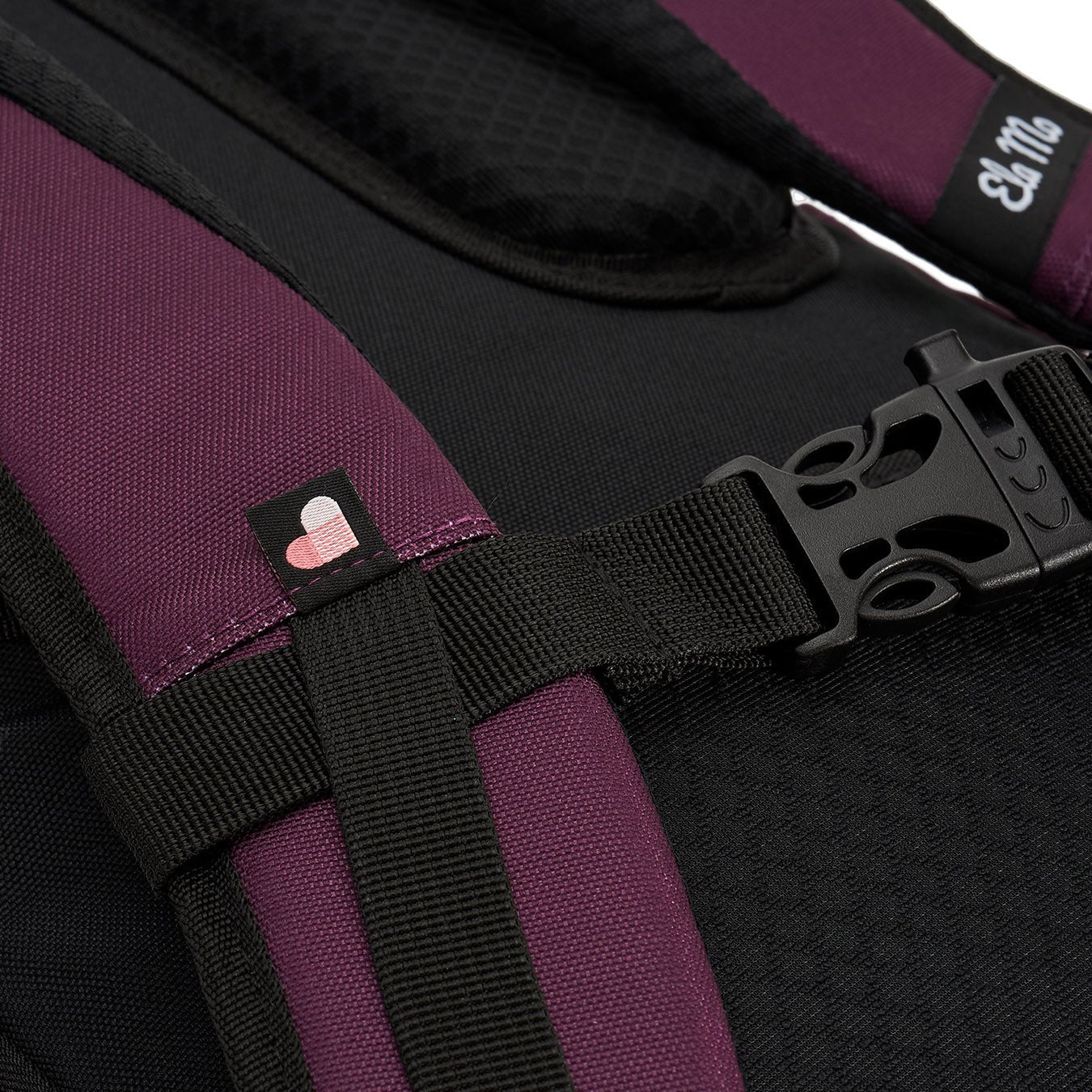 Ela Mo™ Everywhere Daypack | Grape. Schulterriemen mit Schnallenverschluss, Herstellerlogo und kleinem Herzdetail.