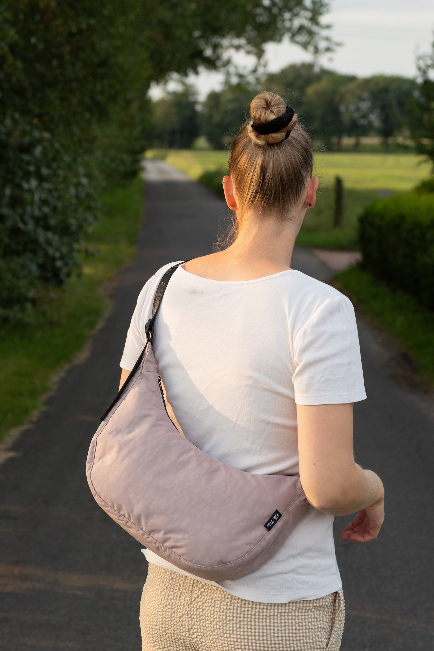 Ela Mo™ Moon Bag | Lavender. Eine Frau mit der Tasche im Sommer auf der Wiese – alltäglicher Lifestyle.