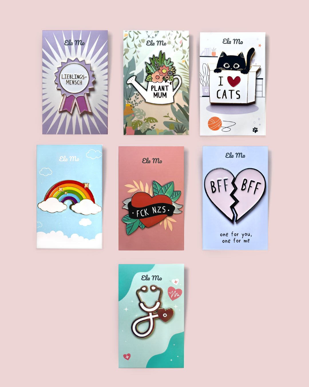 Ela Mo™ Pin für Rucksäcke | Cat. Verschiedene Ausführungen von Rucksackpins auf rosa Hintergrund.