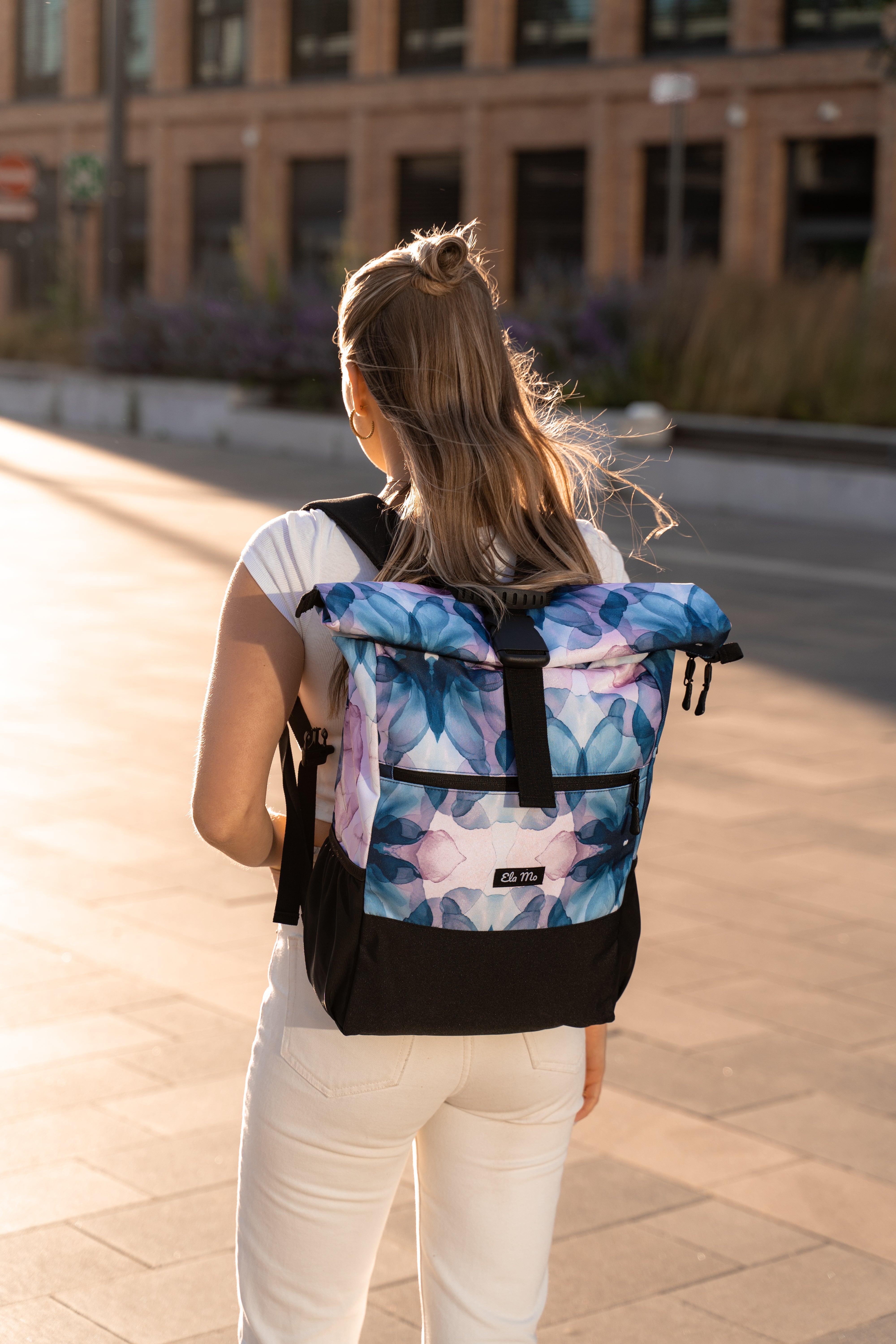 Ela Mo™ Rolltop Rucksack | Aqua. Eine Frau trägt den Rucksack in der Stadt – alltäglicher Lifestyle.