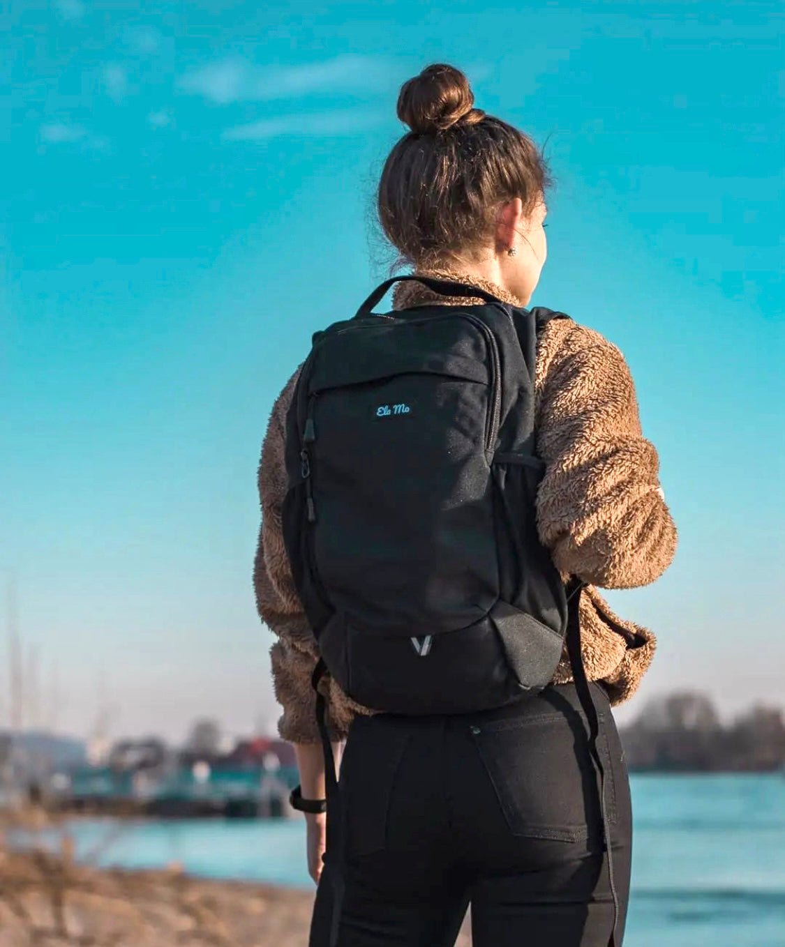 Ela Mo™ Flow Rucksack | Black. Eine Frau mit dem Rucksack auf dem Rücken im Freien.
