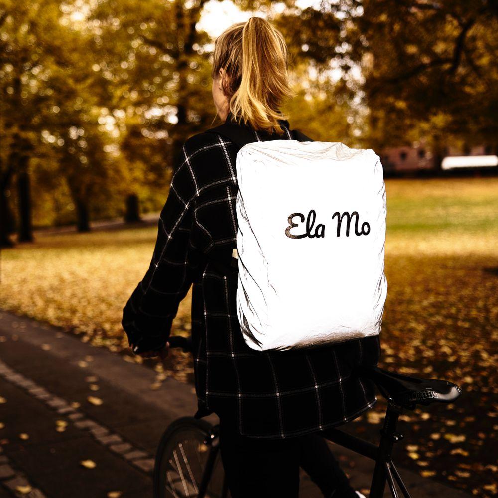 Ela Mo™ Rucksack Regenschutz. Eine Frau mit dem Fahrrad unterwegs, mit Regenschutz auf dem Rucksack.