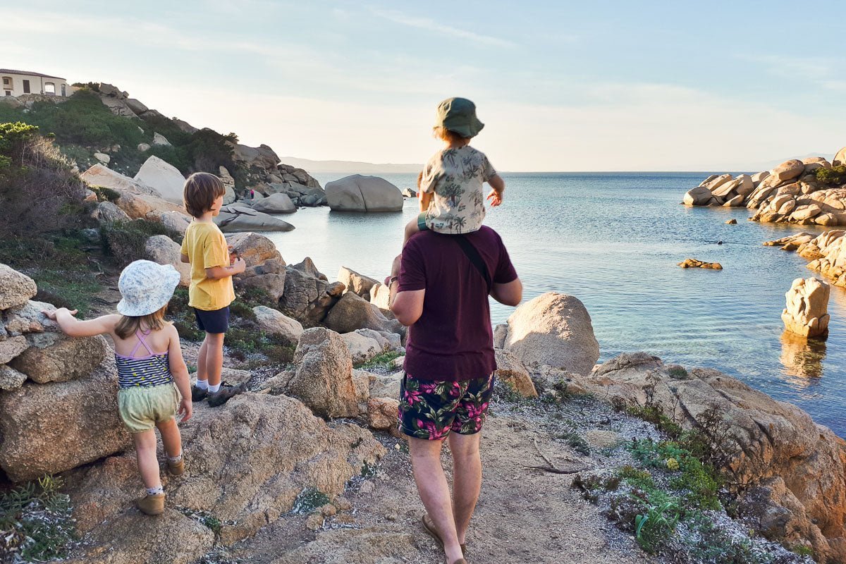 Ein Mann mit drei kleinen Kindern, alle sind sommerlich angezogen und im Hintergrund ist das Meer 