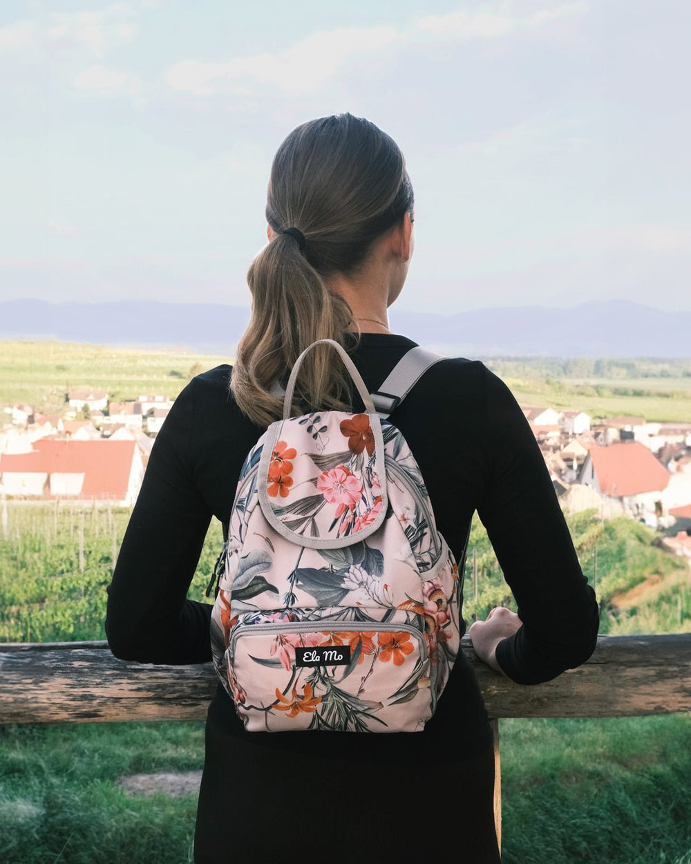 Ela Mo™ Mini Rucksack | Luxe. Eine Frau mit dem Rucksack an einem sonnigen Tag, Ansicht von hinten.