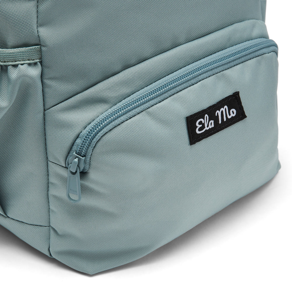 Ela Mo™ Mini Rucksack | Old Mint. Außenfach mit Herstellerlogo auf der Vorderseite des Rucksacks.